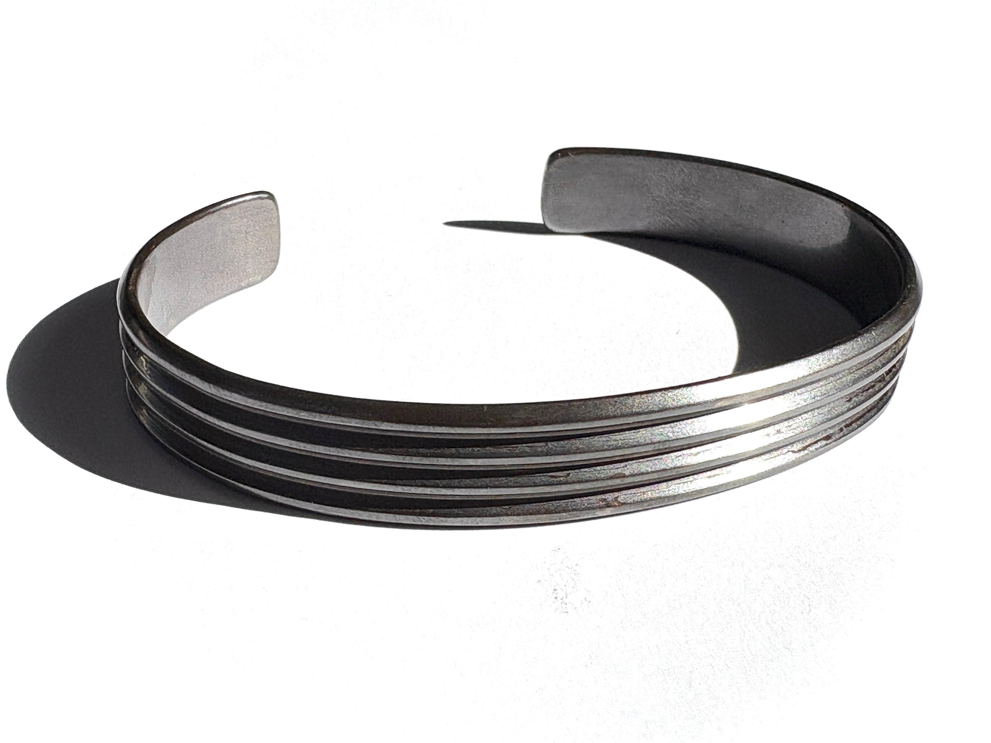 A sterling silver cuff bracelet with a bold, linear pattern, completely oxidized, displayed against a white background.