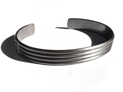 A sterling silver cuff bracelet with a bold, linear pattern, completely oxidized, displayed against a white background.